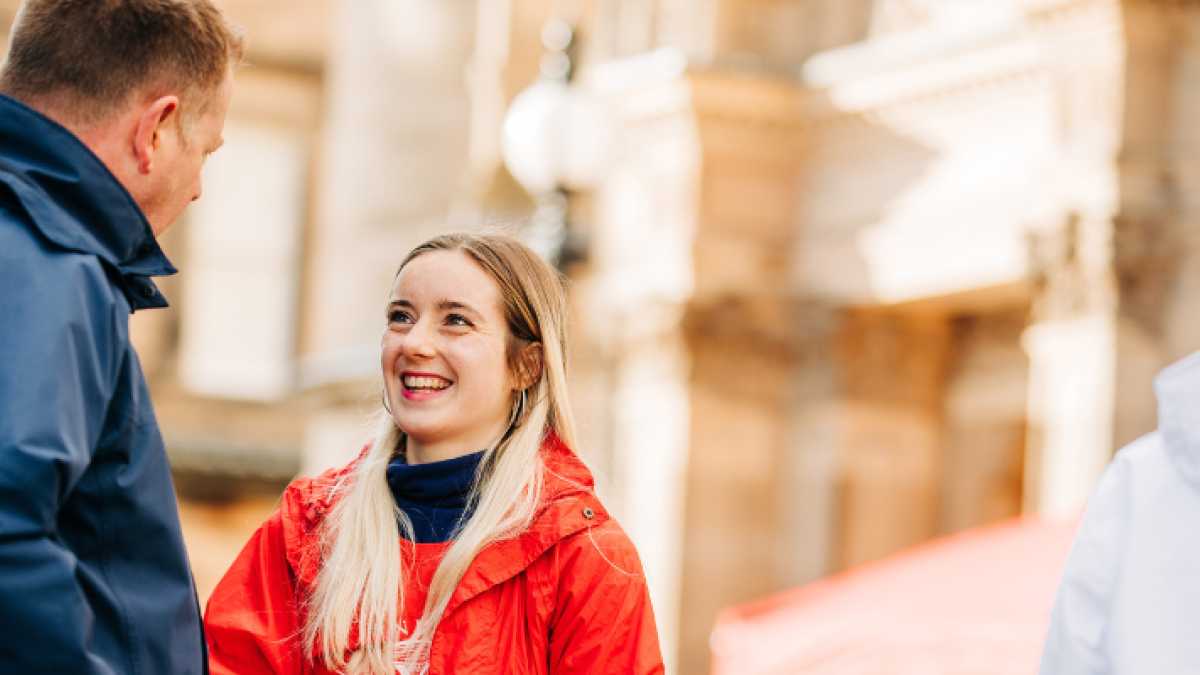 A young open day volunteer in a red coat talks to a visitor