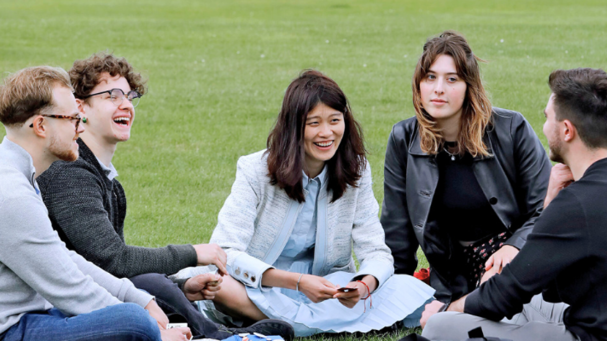 A group of six students six on the grass, talking and laughing