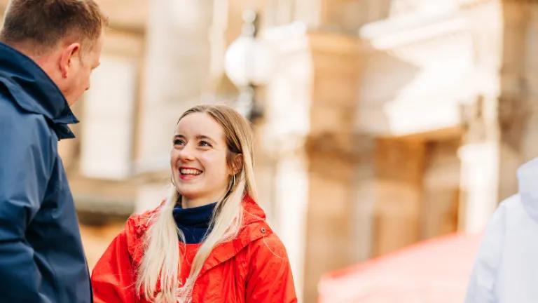 A young open day volunteer in a red coat talks to a visitor